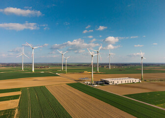 Aerial view of large wind turbines with blades in field against blue sky and white clouds. Alternative energy. Wind farm generating green energy.