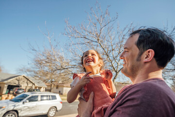 Dad holding happy smiling daughter in front of home