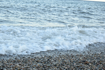 white foam from the waves on the shore, covered with small pebbles of dark color, in the evening
