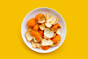 Orange peels in white plate on yellow background.