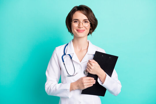 Photo portrait of nurse smiling embracing clipboard wearing white uniform isolated vivid teal color background