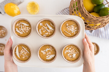 A white ceramic tray held by two woman hands with six bakery cups filled with muffin raw batter and some cocoa slices at the top .