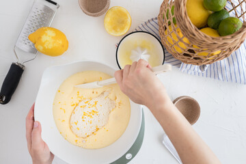 Woman hand mixing with a spatula a muffin batter with lemon shreds at the top.
