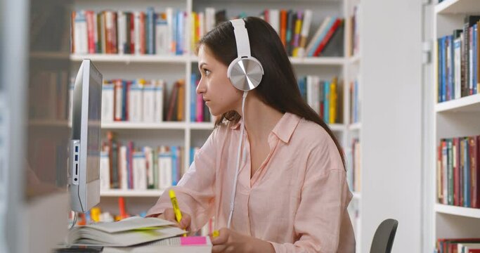 College student wearing headphones having online class on computer sitting at university table.