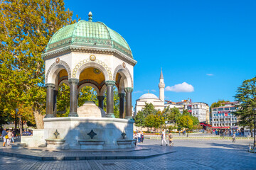 Tourists pass by the German Fountain, a gazebo styled fountain in Sultanahmet Square with the Hagia Sophia in the distance