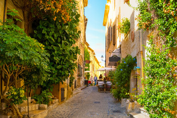 A picturesque back street with tourists enjoying a sidewalk cafe in the medieval hilltop village of Saint-Paul de Vence in the Provence Cote d'Azur region of Southern France.