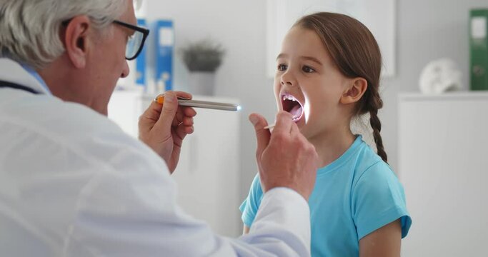 Pediatrician examining little girl throat using spatula and lantern