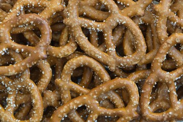 Many salted pretzels scattered loosely, close up directly above. Savory pastry snack traditionally made in Germany and France.