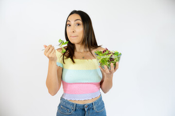 Portrait of a happy playful woman eating fresh salad from a bowl isolated over white background