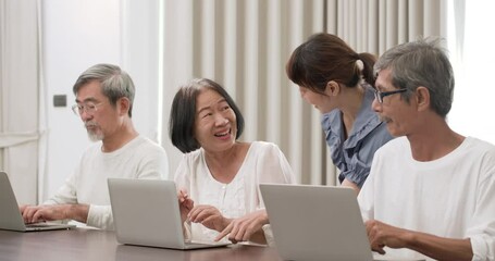 A beautiful kindness young Asian nurse walking around and teaching seniors male and female to using computer in classroom. Teacher take care of older men and women to learn about modern technology.