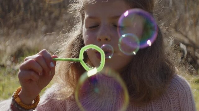Young Girl Blowing Bubbles In Sunlit Field