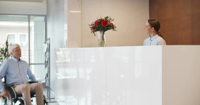 Senior disabled man in wheelchair check-in hotel taking room key from receptionist