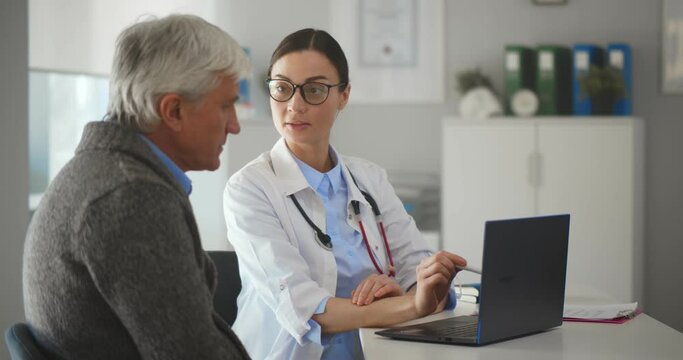 Young doctor talking to senior man patient sitting at desk in hospital office