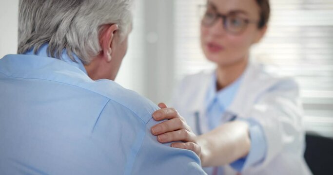 Smiling doctor touching senior man shoulder supporting him and welcoming at clinic