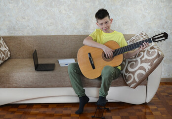teen playing guitar using laptop, home education online, concept of online music courses