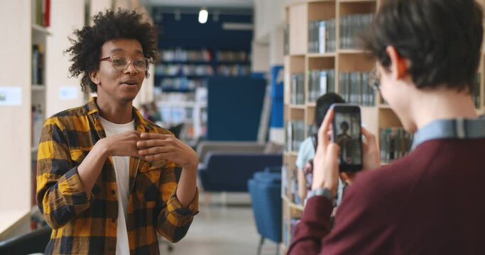Young african blogger recording vlog on digital smartphone cam in library.