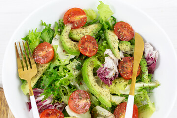 Fresh green salad with avocado, tomatoes, goat cheese in big white bowl on wooden tray. Vegan salad with green mix leaves  and vegetables. Top view on gray table. Healthy vegetarian food. Close up