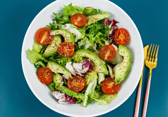 Fresh green salad with avocado, tomatoes, goat cheese in big white bowl on wooden tray. Vegan salad with green mix leaves and vegetables. Top view on blue table. Healthy vegetarian food. Close up	