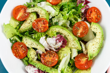 Fresh green salad with avocado, tomatoes, goat cheese in big white bowl on wooden tray. Vegan salad with green mix leaves and vegetables. Top view on blue table. Healthy vegetarian food. Close up	