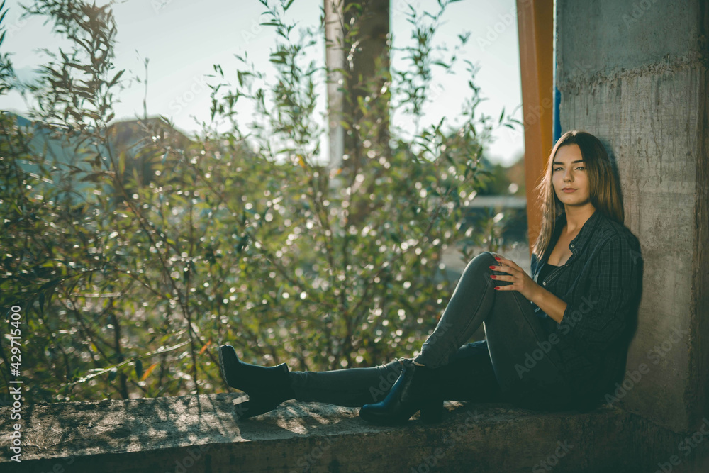 Poster attractive bosnian caucasian woman sitting and leaning against a wall of an abandoned building