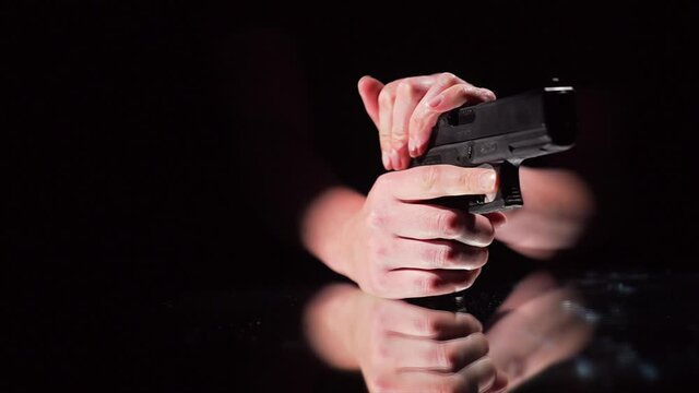 This super slow motion video shows a gun being cocked by anonymous hands as a bullet shell flies out, against a black background.