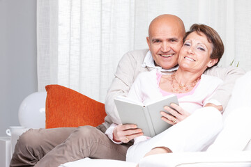 Happy couple relaxing on a sofa together reading a book