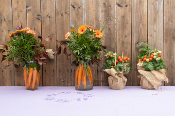 Bio organic original design bouquet with flowers and carrots and Ripe Cherry Tomato Growing In A Pot on table