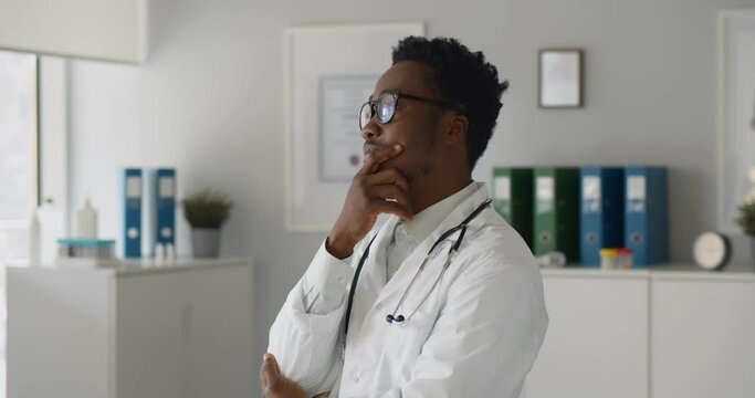 Thoughtful afro-american confident doctor standing in office looking away