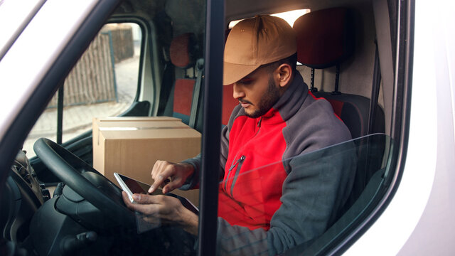 Happy indian courier using tablet in the van . High quality photo