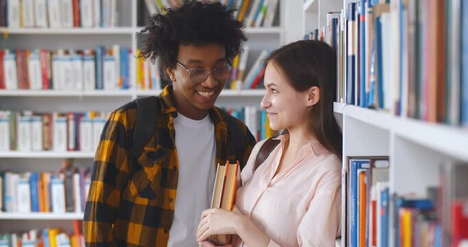 Young multiethnic couple standing against bookshelf in college library