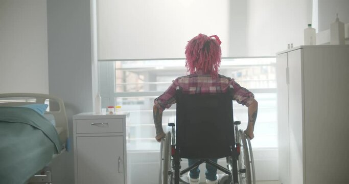 Young woman with pink hair riding in wheelchair in hospital
