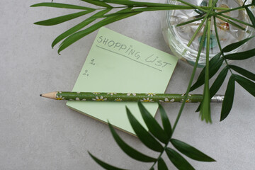 A handwritten shopping list on A Post-it Sticky Notes..Green square shape memo pad..Green leaves and grey background..Organization concept. .Shopping planning concept. - 429719624