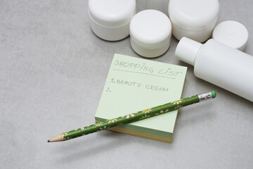 A handwritten shopping list on A Post-it Notes..Blank white plastic bottles and jars for skincare products without labels..Unbranded beauty product package..Grey background..Shopping planning concept. - 429719641