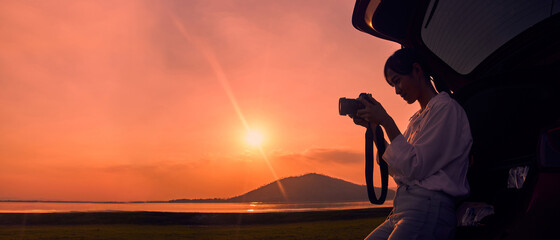 Woman holding a camera in the back of the car at sunset on the lake.