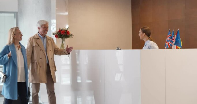 Happy mature couple with luggage and receptionist at counter in hotel