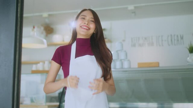asian attractive female cafe staff wear uniform apron smiling cheerful welcome to cafe restaurant with confident and happiness with positive service mind after lockdown is over in shopfront entrance