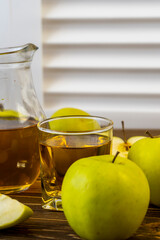 Green apples and jug with glass with apple juice on wooden background