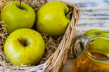 Green apples, basket with apples and jug with apple juice on wooden background