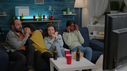 Multi-racial friends screaming while watching thriller horror movie hanging out together on couch. Multi-ethnic people having scary jump reaction and emotions spending time together late at night