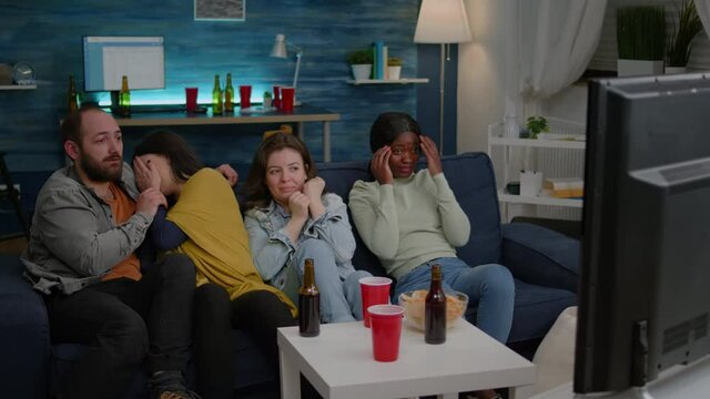 Multi-racial Friends Screaming While Watching Thriller Horror Movie Hanging Out Together On Couch. Multi-ethnic People Having Scary Jump Reaction And Emotions Spending Time Together Late At Night