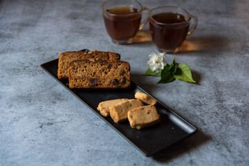 Sliced cake and biscuits on a black tray and tea. Selective focus.