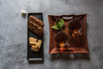 View from top of  Sliced cake and biscuits on a black tray and tea. Selective focus.