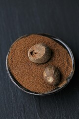 Nutmeg. Whole nutmeg and nutmeg powder in a black  cup on a black slate background.Spices and seasonings.Seasoning for cooking meat and pastries