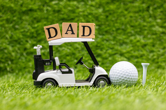 Golf cart with word dad and golf ball are on green grass