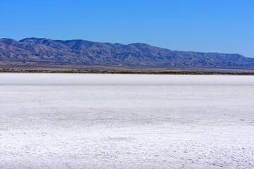 Obraz premium White salt flats of dry Soda Lake at Carrizo Plain National Monument. Temblor Range mountains on horizon on hot and sunny day