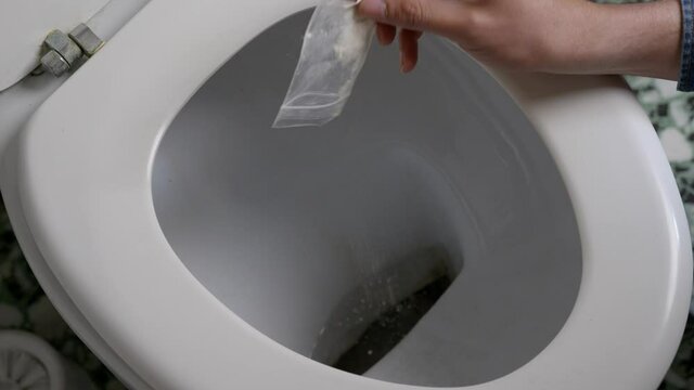 Hand Pouring Out Cocaine Into Toilet Bowl In Restroom Before Flushing. close up, high angle