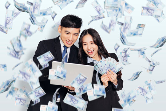 Excited young business man and woman holding laptop with dollars under money rain