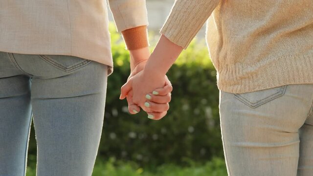 Beautiful romantic moment between two lesbian lovers. Close-up of hands joining together with sunlight flare in the background. Female couple holding hands. LGBT Pride Month, Gay Pride Symbol