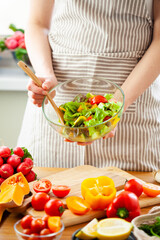 Obraz na płótnie Canvas Beautiful young woman preparing delicious fresh vitamin salad. Concept of clean eating, healthy food, low calories meal, dieting, self caring lifestyle. Colorful vegetables, glass bowl. Close up