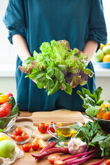 Beautiful young woman holding bouquet of fresh green salad, basil, lettuce. Clean eating, healthy food, low calories meal, dieting, self caring lifestyle. Vegetables from market on a table. Close up